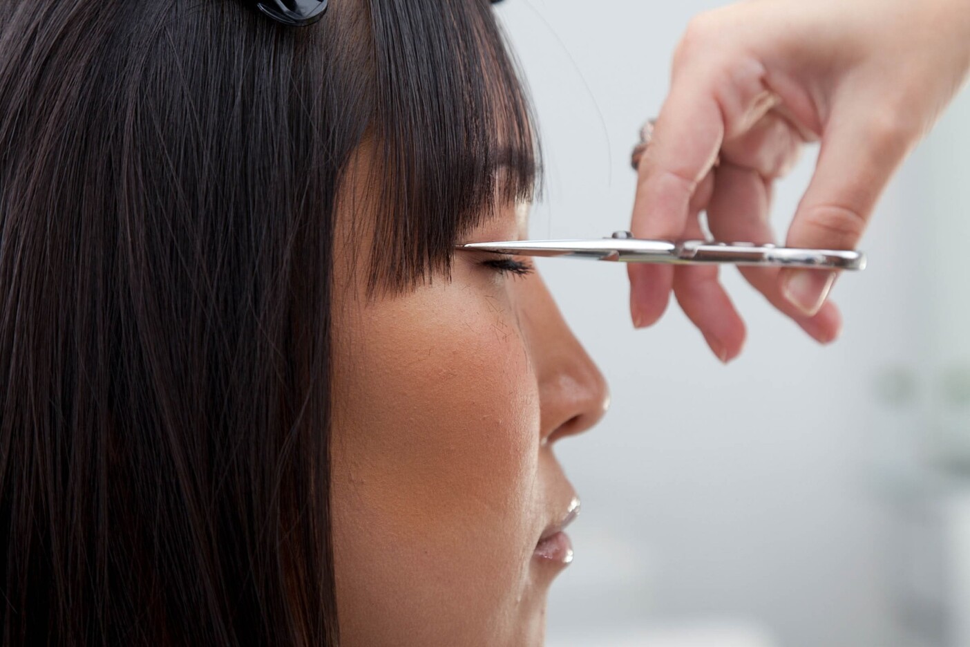 Precision Cut Post Header 2400 x 1600_edited Close-up of a person getting their bangs trimmed by a hairdresser at a popular hair salon. The hairdresser's hand, holding a pair of scissors, is carefully cutting the hair near the person's forehead. The person's eyes are closed during the precise process.