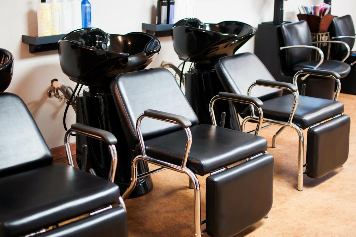 Discover the Path to a Cosmetology License Blog Post Header 2400 x 1600_edited A row of modern black salon chairs with footrests in front of washbasins creates a sleek, inviting path to cosmetology excellence. The clean and organized setup features shelves brimming with hair products, echoing the dedication needed to earn a cosmetology license.