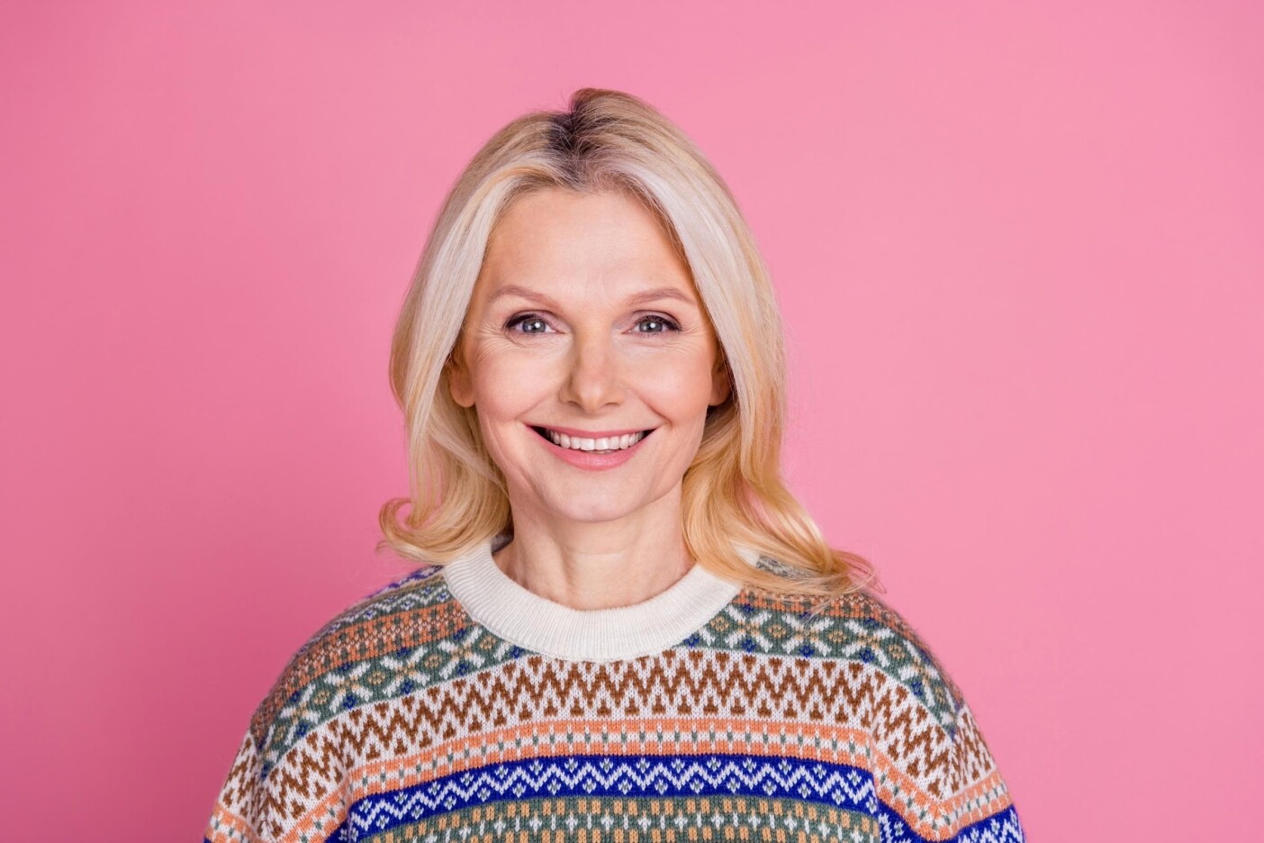 how long does grey coverage last Blog Post Header 2400 x 1600_edited A smiling woman with long blonde hair, showcasing her stylish patterned sweater, stands gracefully against a pink background, leaving one to wonder: how long does grey coverage last for maintaining such vibrant locks?