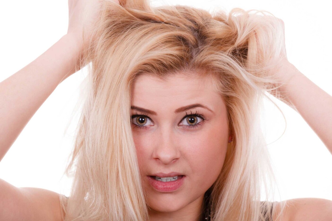 A young person with long blonde hair appears frustrated, holding their hair with both hands. The background is plain white, and they are looking directly at the camera with a concerned expression. Perhaps a visit to one of the best hair salons in Cary, NC is in order!