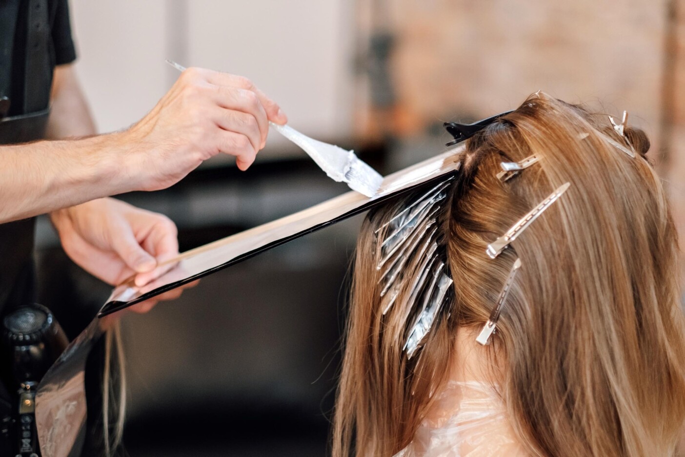 Airtouch technique. Hair stylist dyes hair A hair colorist applies dye with a brush to a client's long hair, carefully sectioned with clips and foil for highlights. The client is wearing a protective cape.