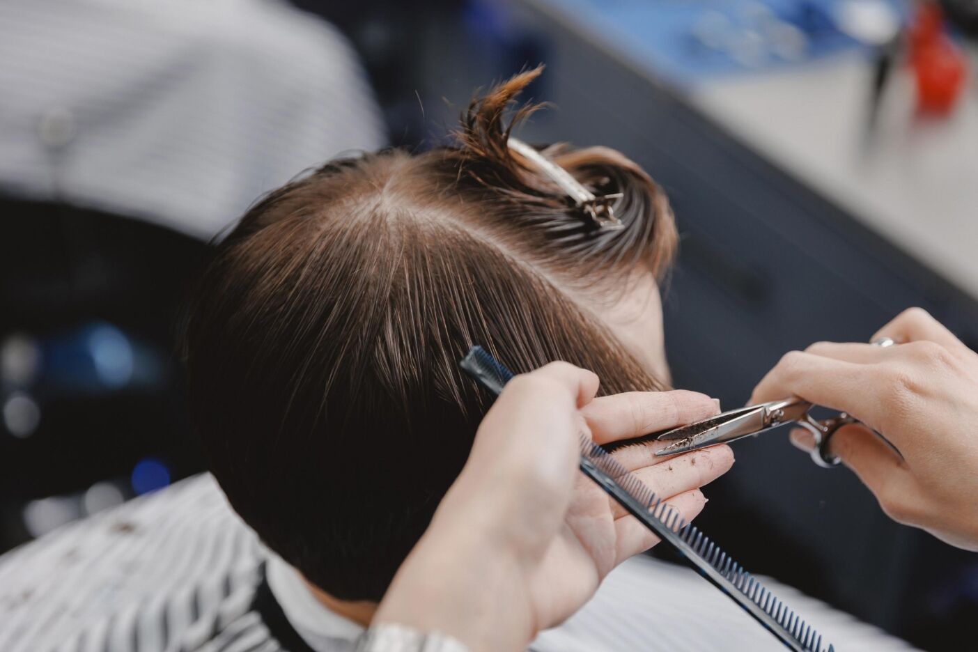 A hairdresser, chosen with care, uses scissors and a comb to trim a person's brown hair in a salon, with hair sectioned and clipped on top—highlighting the importance of choosing a hair stylist you trust.